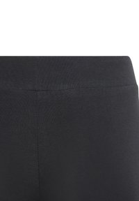 Leggings negros con cintura elástica y textura suave. Presentan un diseño ajustado y un acabado sin costuras en la cintura y la parte posterior.