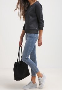 Svart sweatshirt med en slät yta, kombinerad med ljusblå skinny jeans. Neutrala grå sneakers och en svart totebag fulländar looken.