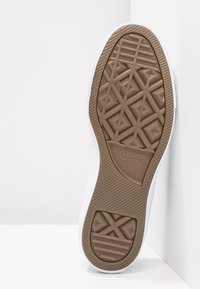 Kumipohjallinen tennari ruskeana, jossa on pintakuvioitu, geometrinen muotoilu. Valkoinen yläreuna ja brändilogo, jossa lukee "Converse ALL STAR."