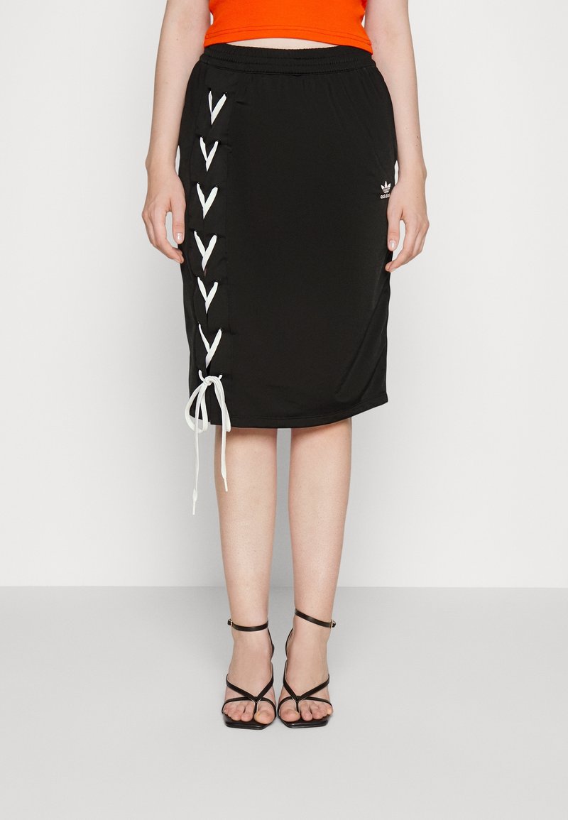 Donna che indossa una gonna nera a lunghezza ginocchio con dettagli in pizzo bianco sui lati, un top arancione e sandali neri con tacchi alti e cinturini.