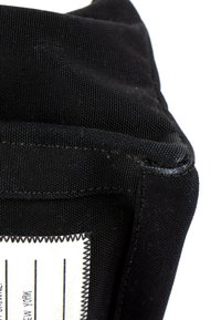 Gros plan d'un coin d'un sac en tissu noir montrant une couture texturée et une étiquette blanche partiellement visible avec des lignes et du texte.