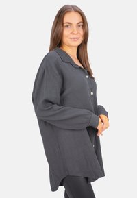 Dark gray oversized shirt made of textured fabric, featuring a collar, button closure, and long sleeves. The hem is slightly curved.
