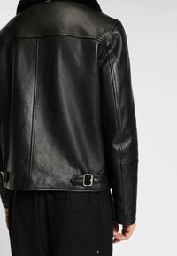 Schwarze Lederjacke mit glatter Textur, ausgestattet mit einem Schafsfell-Kragen und verstellbaren Schnallen-Details am Saum und an den Ärmeln.