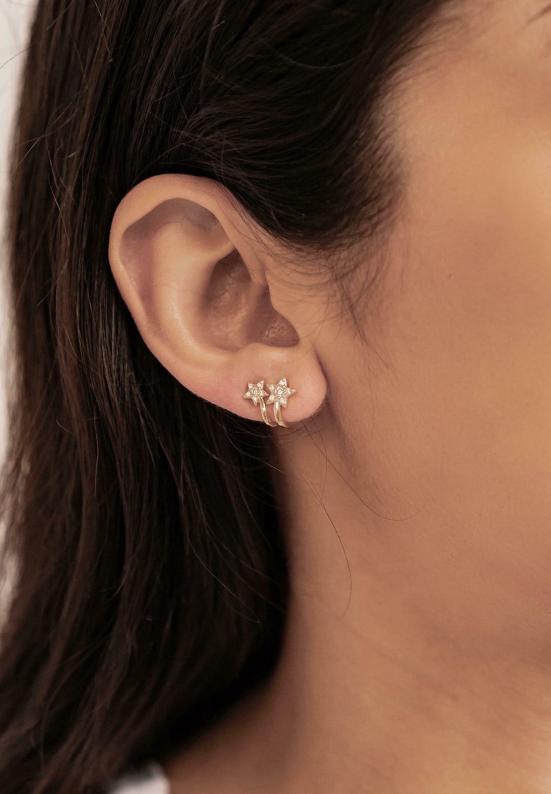 Silver star-shaped earrings with small clear gemstones, featuring a delicate hoop design attached to the earlobe.