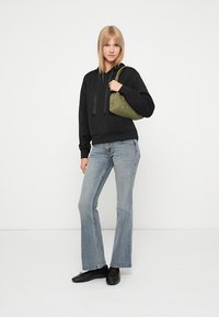 Svart hettegenser, lyseblå utsvungne jeans og svarte sko. Modellen bærer en olivengrønn veske med dekorative detaljer.