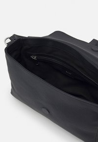 Czarna skórzana torba o fakturowej powierzchni, z dużym otworem i wewnętrzną kieszenią na zamek błyskawiczny. Wnętrze wyłożone jest czarnym materiałem.