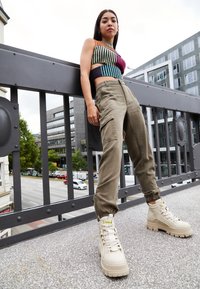 Haut court en maille colorée à rayures horizontales, pantalon cargo vert olive et baskets à plateforme beiges épaisses avec lacets.