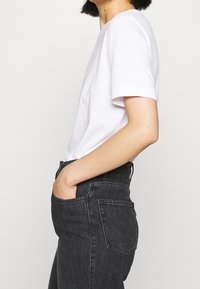 Witte t-shirt met korte mouwen en een relaxte pasvorm, gecombineerd met high-waisted donkerdenim jeans. De jeans hebben gestikte zakdetails.