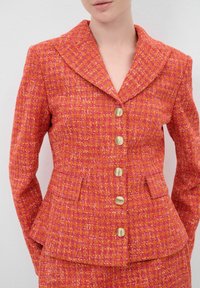 Texturiertes, rosa-orange Blazer mit goldenen Knöpfen, einem spitzen Kragen und einer taillierten Taille. Mit zwei Fronttaschen und einem Peplum-Saum.