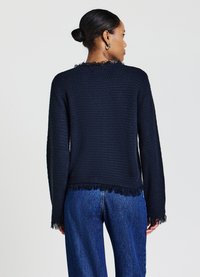 Maritimer, strukturierter Pullover mit fransigem Saum und Bündchen, langen Ärmeln und rundem Ausschnitt. Kombiniert mit hellblauer Jeans.
