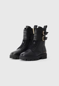 Sorte lær ankle boots med snørelukking foran, lynlås på siden, to justerbare stropper med gullspenner og tung såle.