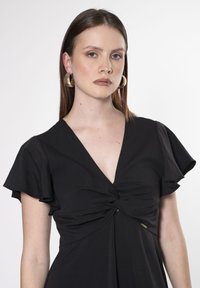 Vestido negro con un escote en V profundo, mangas ligeras y un detalle de nudo recogido en la cintura. Textura de tela suave con un brillo sutil.