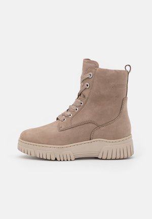 Tan ankle boots made of smooth leather with a lace-up front, metallic eyelets, and a chunky rubber sole with textured tread.