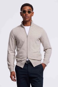 Lichtgrijze zip-up sweater van een zachte gebreide stof; heeft een hoge kraag en ribgebreide cuffs. Gestyled met een wit shirt en donkere broek.