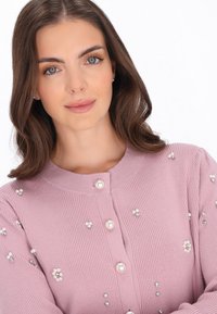 Rózsaszín bordázott kardigángyöngy és rhinestones díszítéssel, kerek nyakú, gombos előlappal. Puha tapintás, testhezálló fazon.