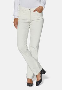 Weiße Baumwollmischung-Hosen mit geradem Bein, fünf Taschen und silbernen Beschlägen. Getragen mit schwarzen, klobigen Absätzen.