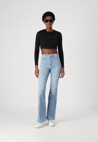 Sort cropped langærmet top med frontknapper, lys blå flagrende jeans og hvide sneakers. Model iført sorte solbriller.