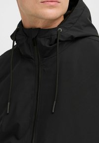 Czarna wodoodporna kurtka z wysokim kołnierzem, regulowanymi sznurkami oraz pełnym zamkiem błyskawicznym; gładka tekstura i elegancki, minimalistyczny design.