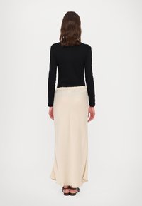 Black long-sleeve top paired with a cream maxi skirt featuring a ruffled waistband, smooth texture, and a slight flare at the hem.