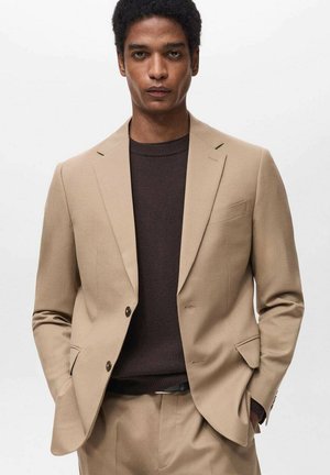Beige maßgeschneiderte Sakko mit Revers, Ein-Knopf-Verschluss und Seitentaschen, getragen über einem dunkelbraunen Pullover. Glatte Stoffoberfläche.
