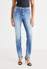 Lichtblauwe denim jeans met een rechte pijp, voorzien van voorzakken, een knoopsluiting en een lichte vervaging. Gemaakt om te dragen met zwarte bandenhakken.