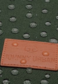 Zöld szövet, kiemelkedő pöttyökkel, vízcseppekkel díszítve. Egy világosbarna bőr címke "JOHNNY URBAN" felirattal, különleges betűtípussal.