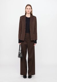 Dark brown tailored blazer and matching wide-leg trousers paired with a black sweater, holding a small black handbag.