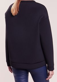 Sweatshirt noir avec une coupe ample, un col rond et des poignets côtelés. Fabriqué à partir d'un matériau doux sans motifs ou accents visibles.