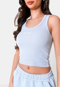 Top corto a coste azzurro chiaro con scollatura rotonda e logo bianco sul petto, abbinato a pantaloni felpati azzurro chiaro coordinati.