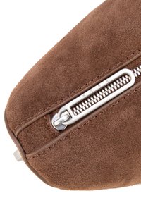 Ecke einer braunen Wildledertasche mit silbernem Reißverschluss, die eine strukturierte Oberfläche und dezente Nähte aufweist. Der Reißverschlussanhänger ist mit einer eingravierten Markendetail versehen.