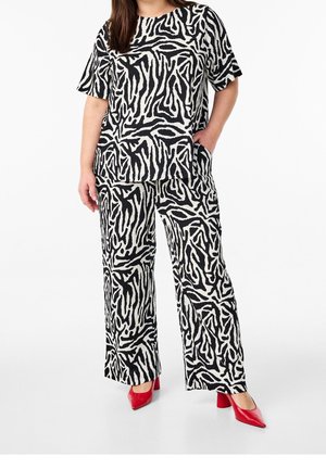 Vrouw in een zwart-witte abstracte print kortebloes met korte mouwen en wijde broek, gecombineerd met rode puntige blokhak schoenen.