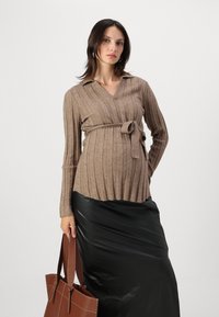 Brauner gerippter Wickel-Pullover mit einem Knoten in der Taille, kombiniert mit einem schwarzen Satinrock und einer braunen Leder-Umhängetasche. Glatte Textur.