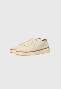 Sneaker crema chiaro con tomaia in knit texture, punta rotonda, sei asole in metallo e suola in gomma cucita marrone a contrasto.