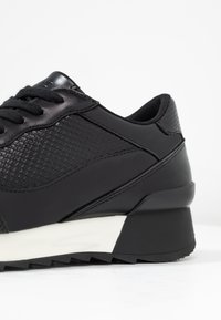 Black athletic shoe featuring a textured upper with a smooth finish, a thick white midsole, and a sturdy black outsole with traction points.