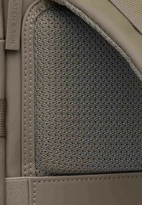 Strukturierter grauer Stoff mit einem gewebten Muster, umrandet von beigem synthetischem Material, mit sauberen Nähten und einem Markenetikett an der Seite.