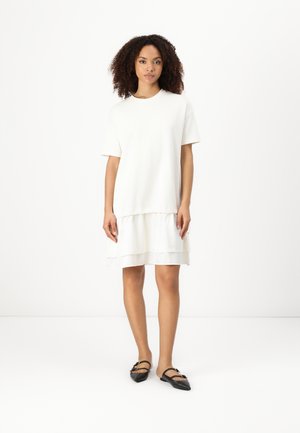 Robe t-shirt blanche à manches courtes, avec un ourlet superposé et une texture douce. Assortie à des chaussures plates noires avec une boucle décorative.