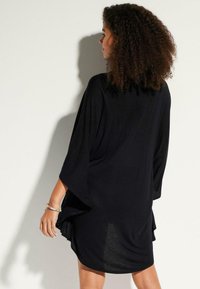 Robe noire à coupe ample avec des manches chauve-souris, fabriquée en tissu doux et texturé, présentant un ourlet arrondi et une silhouette décontractée.