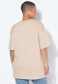 Beige oversized tričko s krátkým rukávem, kulatým výstřihem a lehkým materiálem, spárované s modrými vzorovanými kalhotami.