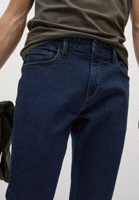 Jeans de mezclilla azul oscuro de ajuste clásico, con cremallera, cinco bolsillos y detalles de costura en naranja.