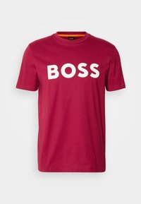 T-shirt rouge foncé à manches courtes avec col rond et texte blanc en gras "BOSS" sur la poitrine, sur un fond uni clair.