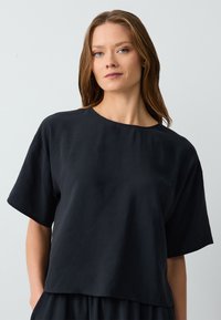 Top nero a maniche corte realizzato in un tessuto morbido. Presenta un colletto rotondo e una vestibilità rilassata, con un leggero taglio corto.