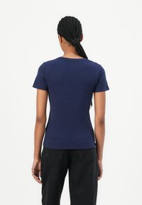 T-shirt à manches courtes bleu marine en tissu doux et extensible. Doté d'un col rond et d'une coupe ajustée. Associé à un pantalon noir.