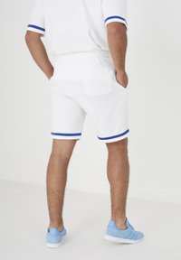 Shorts bianchi con texture e strisce azzurre, dotati di vita elastica e tasca posteriore. Abbinati a sneakers azzurre chiare.