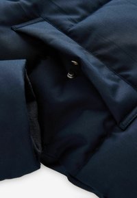 Interiorul unui geacă căptușită de culoare albastră marină, cu o textură netedă, având închidere cu capse și o căptușeală din tricot moale expusă în partea de jos.