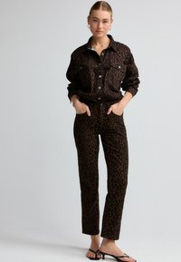 Veste chemise en imprimé léopard brun avec des boutons sur le devant et deux poches poitrine, assortie à un pantalon en imprimé léopard brun. Texture du tissu lisse.