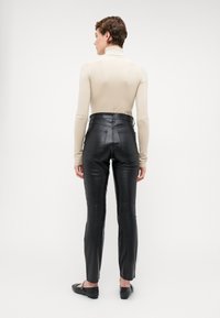 Svarta läderbyxor med hög midja, en åtsittande design och raka ben, tillsammans med en beige polotröja. Inga synliga mönster eller detaljer.