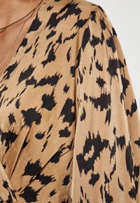 Leopardi kuosisettu kietaisumekko, jossa on silkkinen pinta, vaaleanruskea pohjaväri mustilla pilkuilla ja roikkuvat hihat, jotka luovat kevyen siluetin.