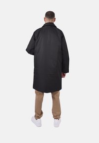 Cappotto nero fino al ginocchio con vestibilità rilassata, caratterizzato da una linea dritta, maniche lunghe e colletto classico, realizzato in tessuto morbido.