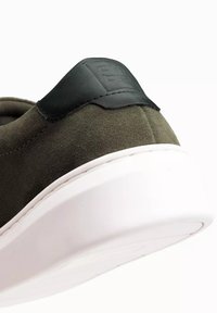 Sneaker en suède vert olive avec un accent de talon en cuir noir et une semelle en caoutchouc blanc. Doté d'une surface texturée et de détails cousus.