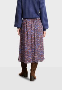 Lång, mönstrad kjol i nyanser av brunt, blått och rött; tillverkad av lätt material med dragsnodd i midjan, i kombination med bruna mocka knästövlar.